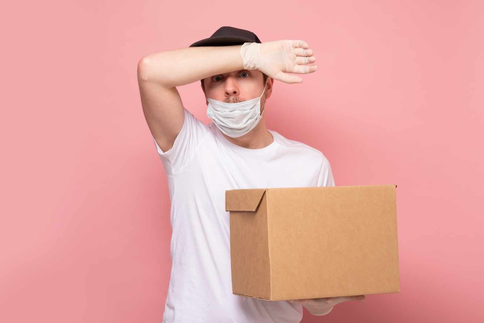 tired caucasian man is holding a heavy box, wiping the sweat.