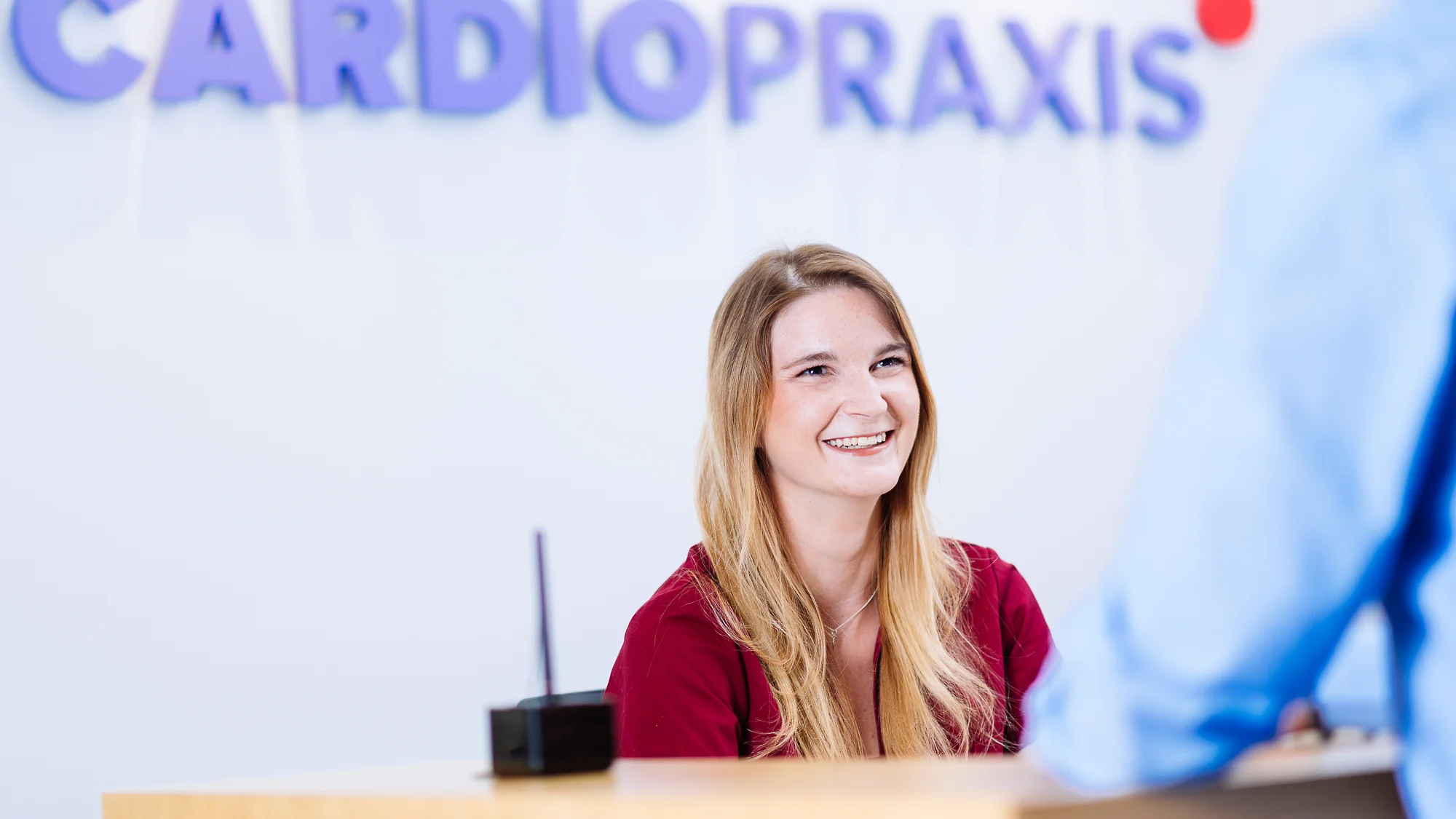 Lächelnde Frau an Rezeption einer Kardiopraxis