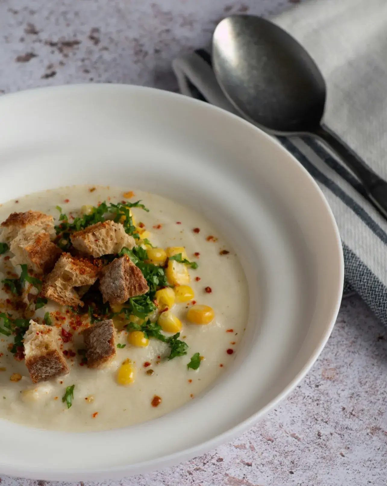 Suppe mit Mais, Croutons und Petersilie serviert